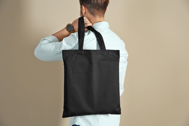 Young man holding textile bag on color background, closeup. Mockup for design