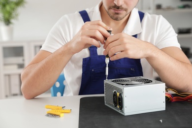 Photo of Male technician repairing power supply unit at table indoors, closeup