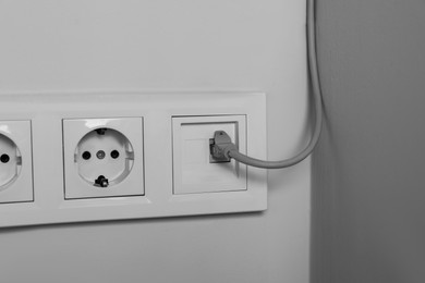 Power sockets with internet cable on white wall, closeup. Electrical supply