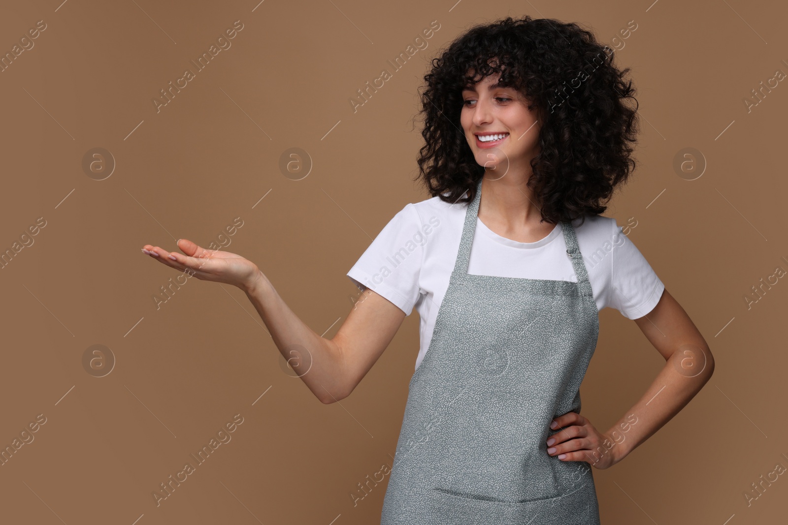 Photo of Happy woman wearing kitchen apron on brown background. Mockup for design