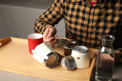 Man putting ground coffee into moka pot at table indoors, closeup