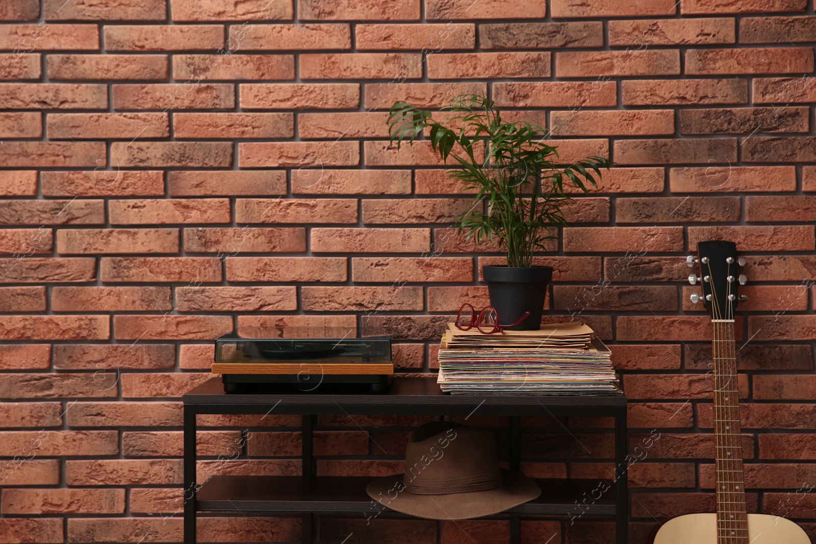 Photo of Stylish turntable and vinyl records on shelving unit near red brick wall