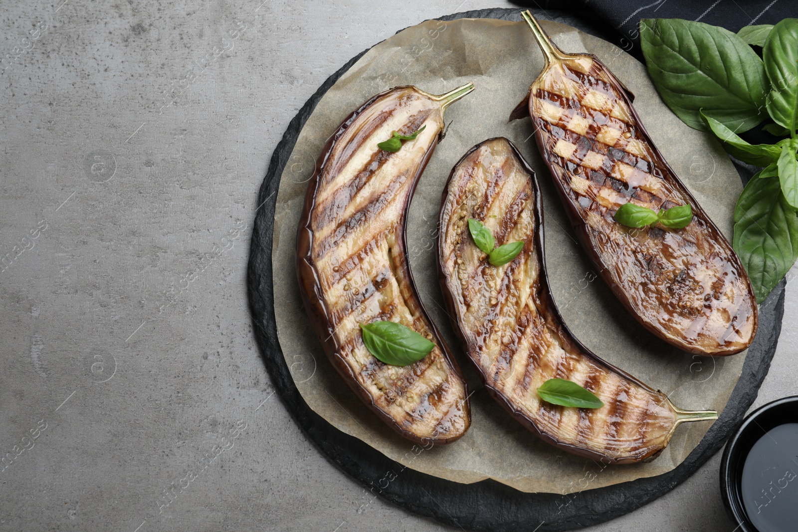 Photo of Delicious grilled eggplant halves with basil served on grey table, flat lay. Space for text