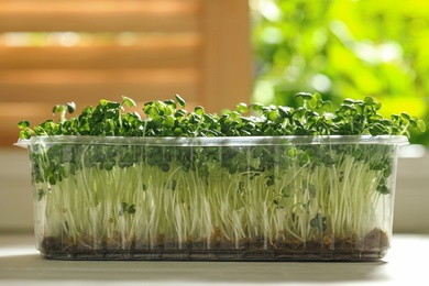 Photo of Sprouted arugula seeds in plastic container on white wooden table