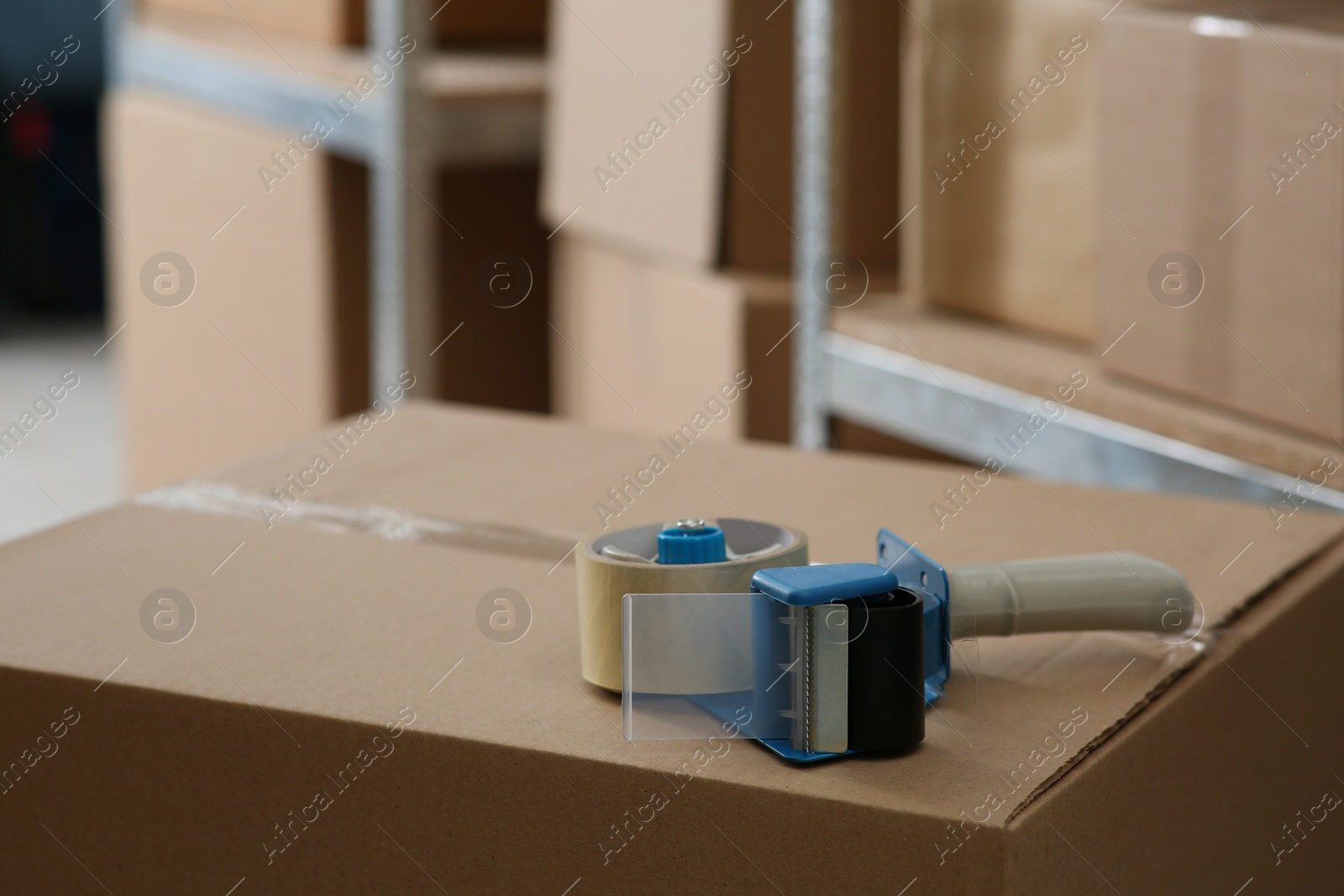 Photo of Adhesive tape dispenser on cardboard box indoors