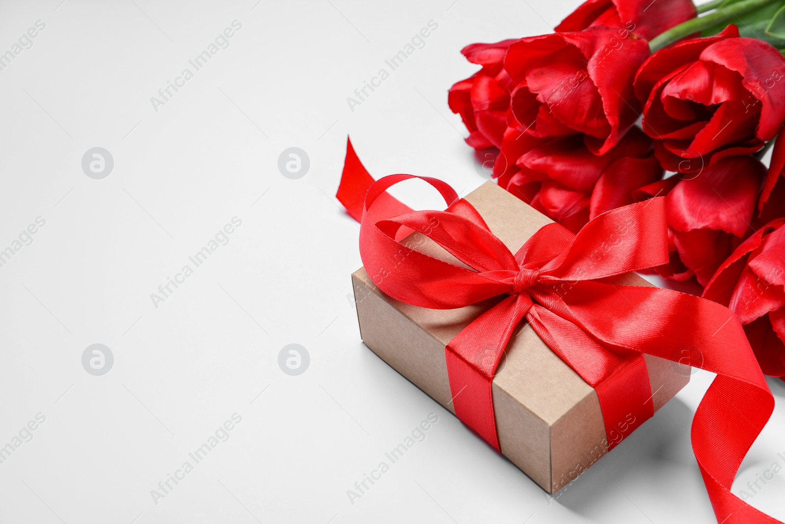 Photo of Beautiful gift box with bow and red tulip flowers on white background. Space for text