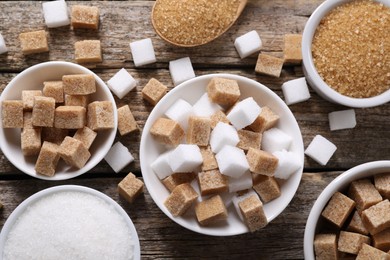 Different types of sugar in bowls on wooden table, flat lay