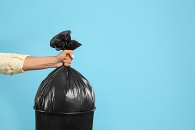 Woman taking garbage bag out of bin on light blue background, closeup. Space for text