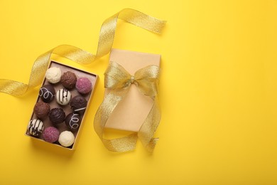 Photo of Open box with delicious chocolate candies and ribbon on yellow background, top view. Space for text