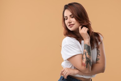 Photo of Beautiful tattooed woman on beige background, space for text