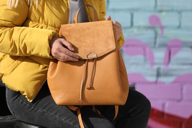 Young woman with stylish backpack near brick wall outdoors, closeup