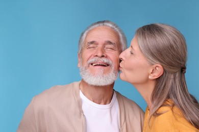Photo of Senior woman kissing her beloved man on light blue background, space for text