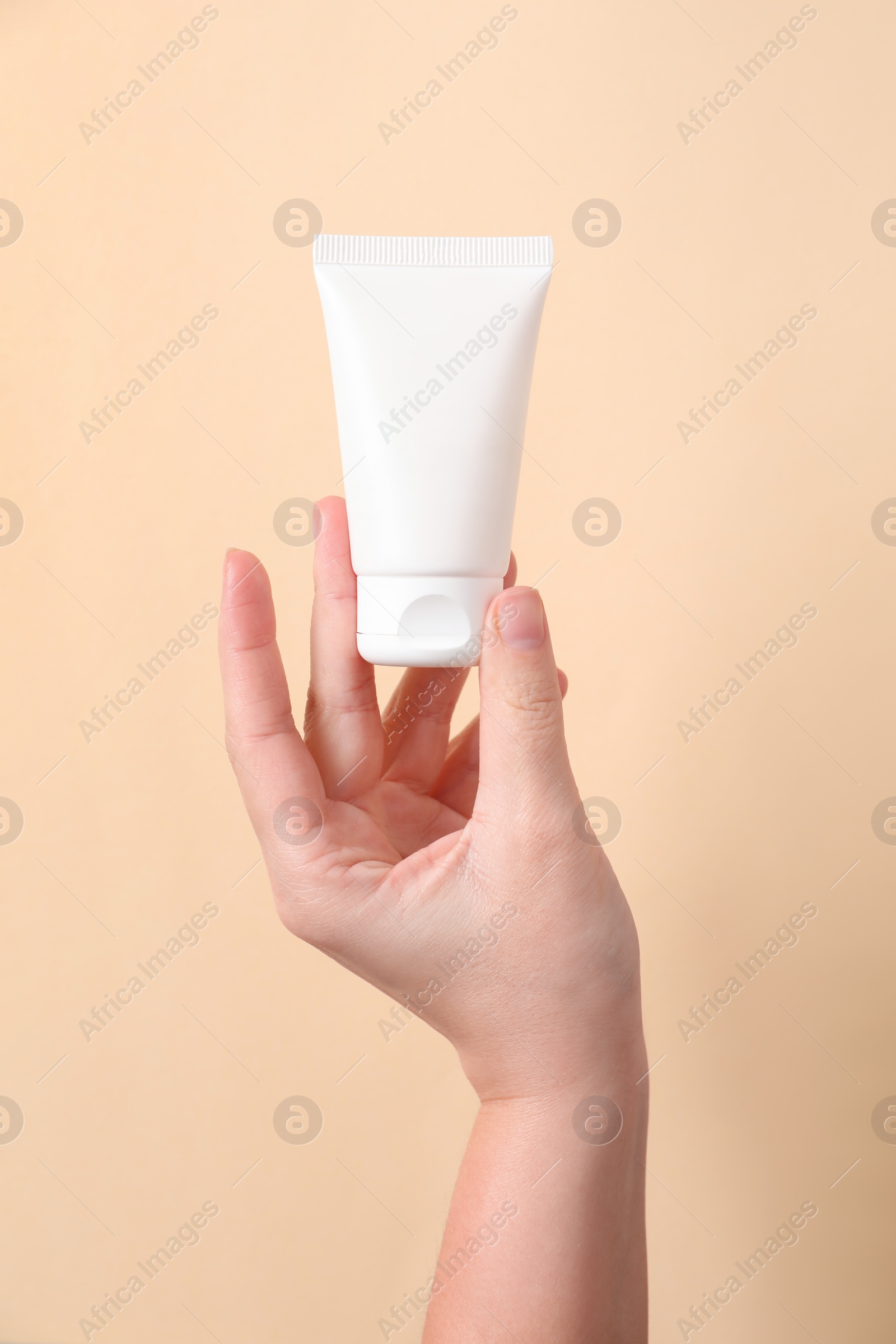 Photo of Woman with tube of hand cream on beige background, closeup