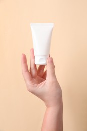 Photo of Woman with tube of hand cream on beige background, closeup