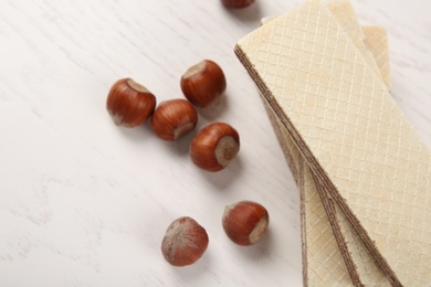 Photo of Delicious wafers with hazelnuts on white wooden background, top view