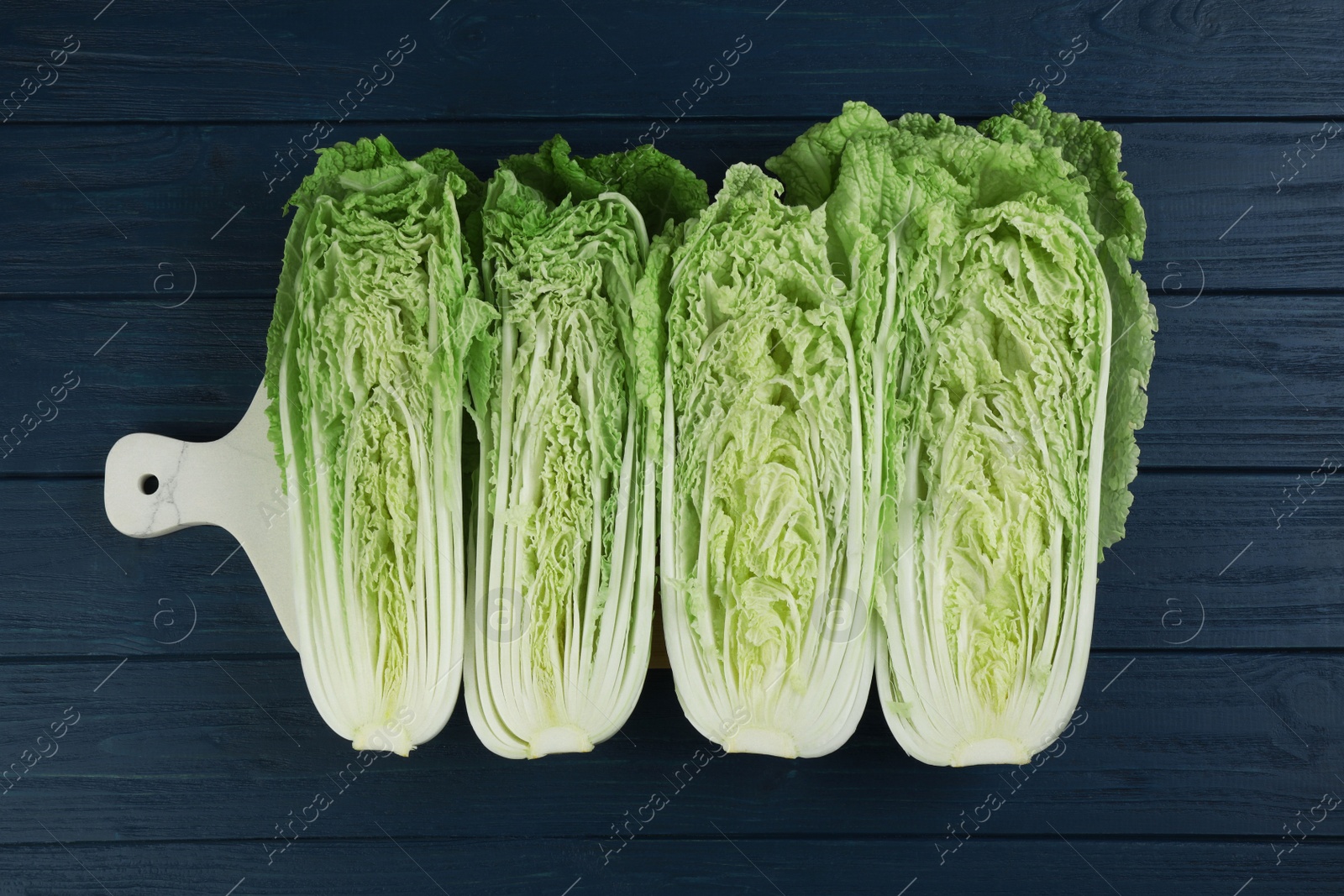 Photo of Cut fresh ripe Chinese cabbages on blue wooden table, flat lay