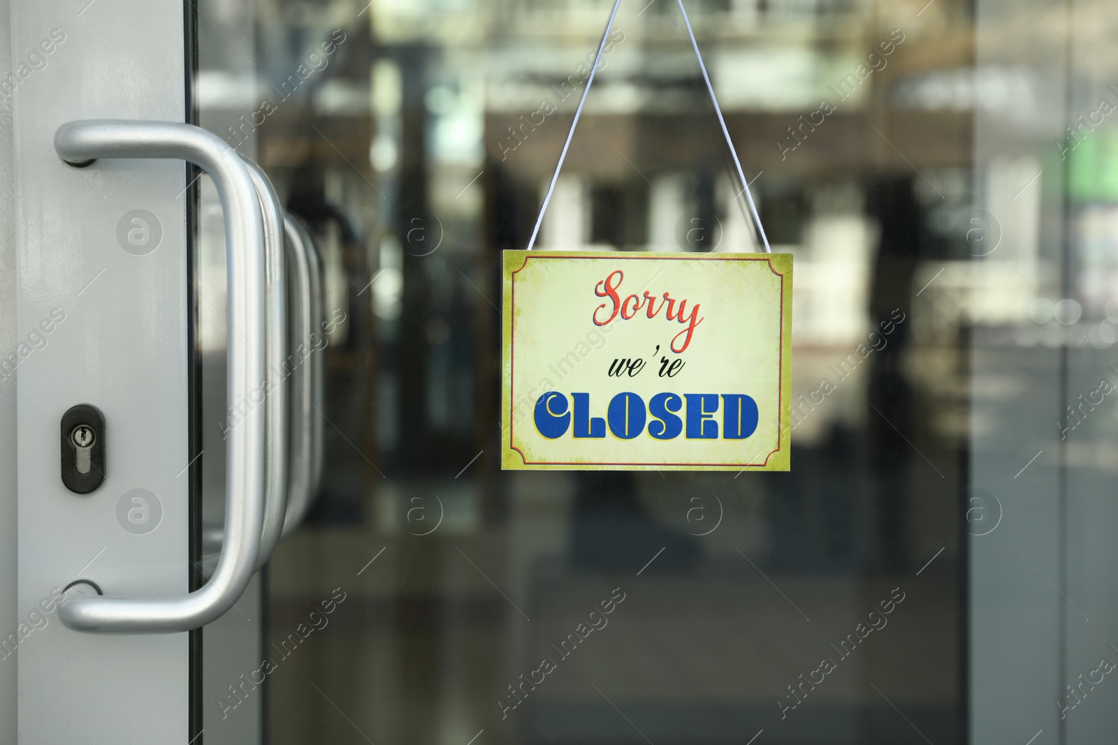 Photo of Yellow sign with text Sorry we're Closed hanging on glass door. Coronavirus quarantine