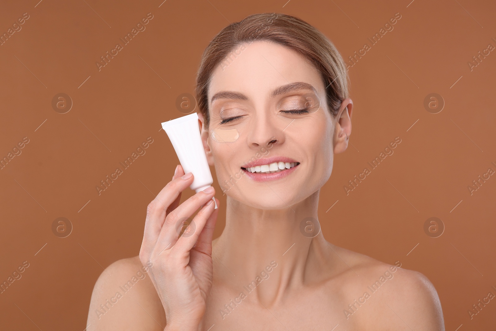 Photo of Woman holding tube of foundation on brown background