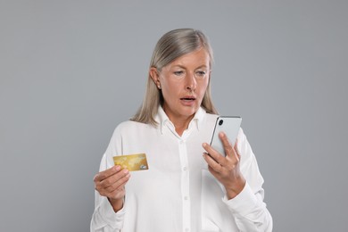 Photo of Worried woman with credit card and smartphone on light grey background. Be careful - fraud