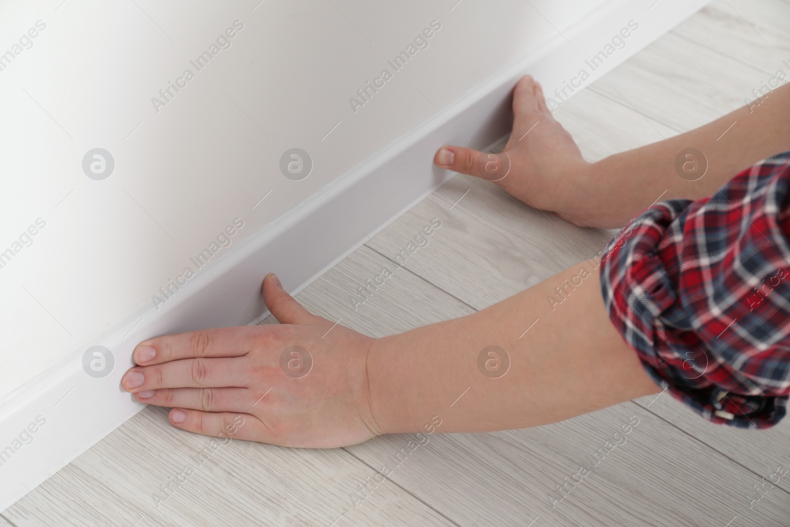 Photo of Man installing plinth on laminated floor in room, closeup