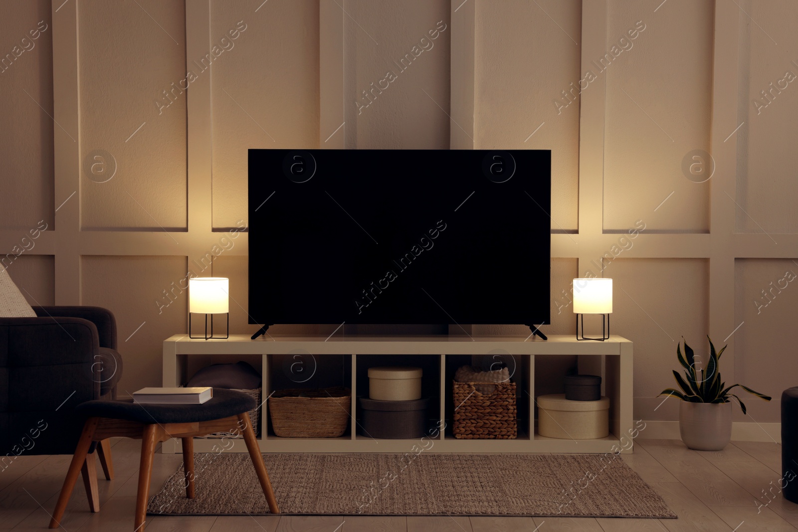 Photo of Modern TV on cabinet, armchair and lamps indoors. Interior design