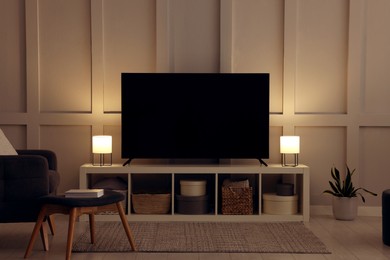 Modern TV on cabinet, armchair and lamps indoors. Interior design