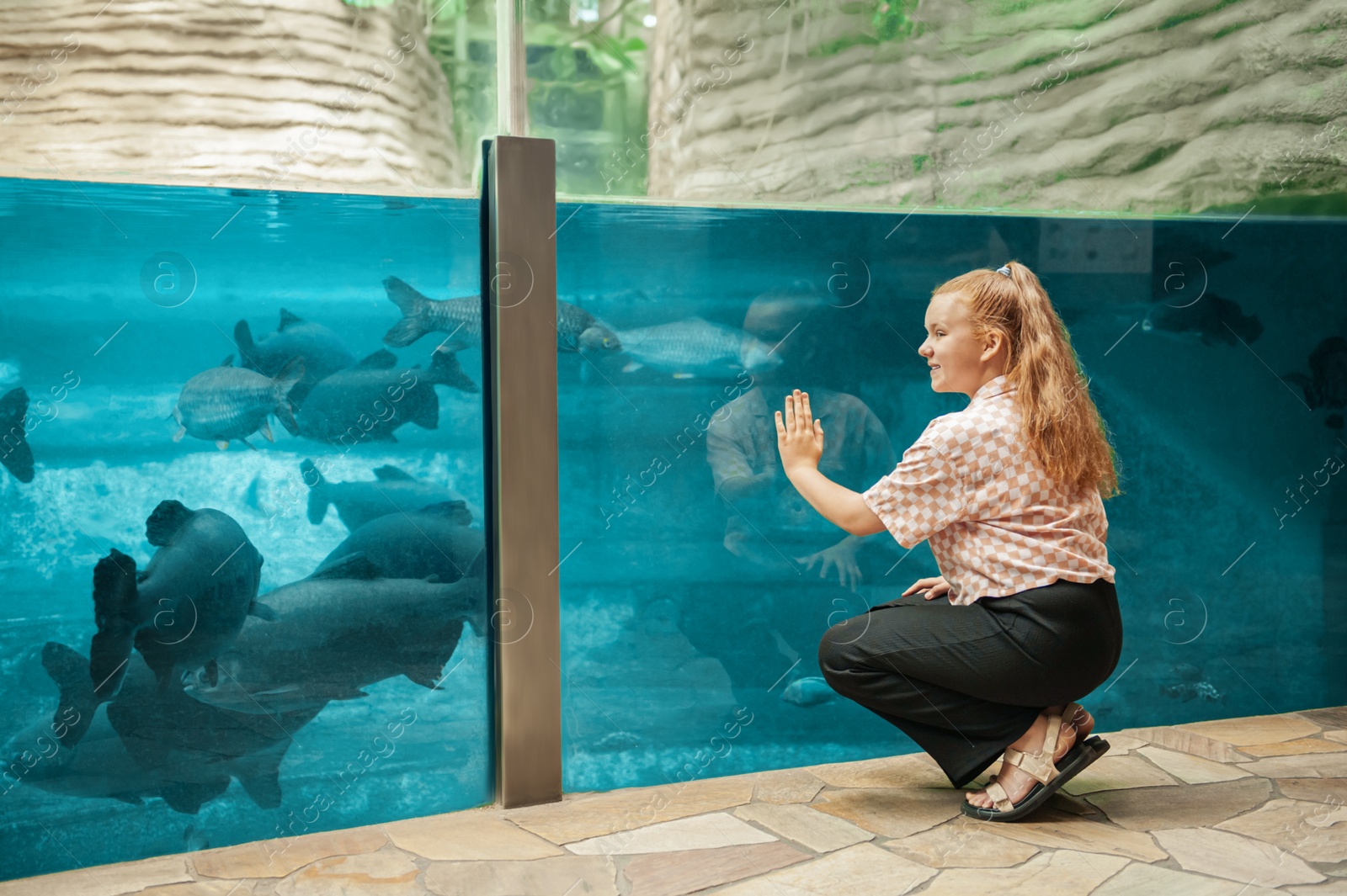 Photo of Cute girl sitting near large aquarium in oceanarium