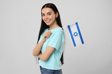 Happy young woman with flag of Israel on beige background