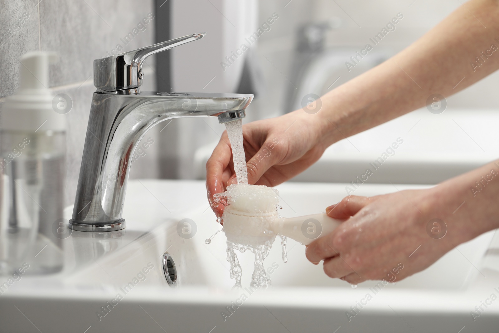 Photo of Young woman washing facial brush in bathroom, closeup