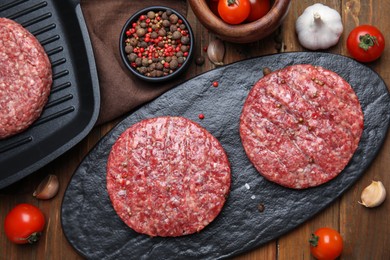 Photo of Raw hamburger patties with pepper and vegetables on wooden table, flat lay