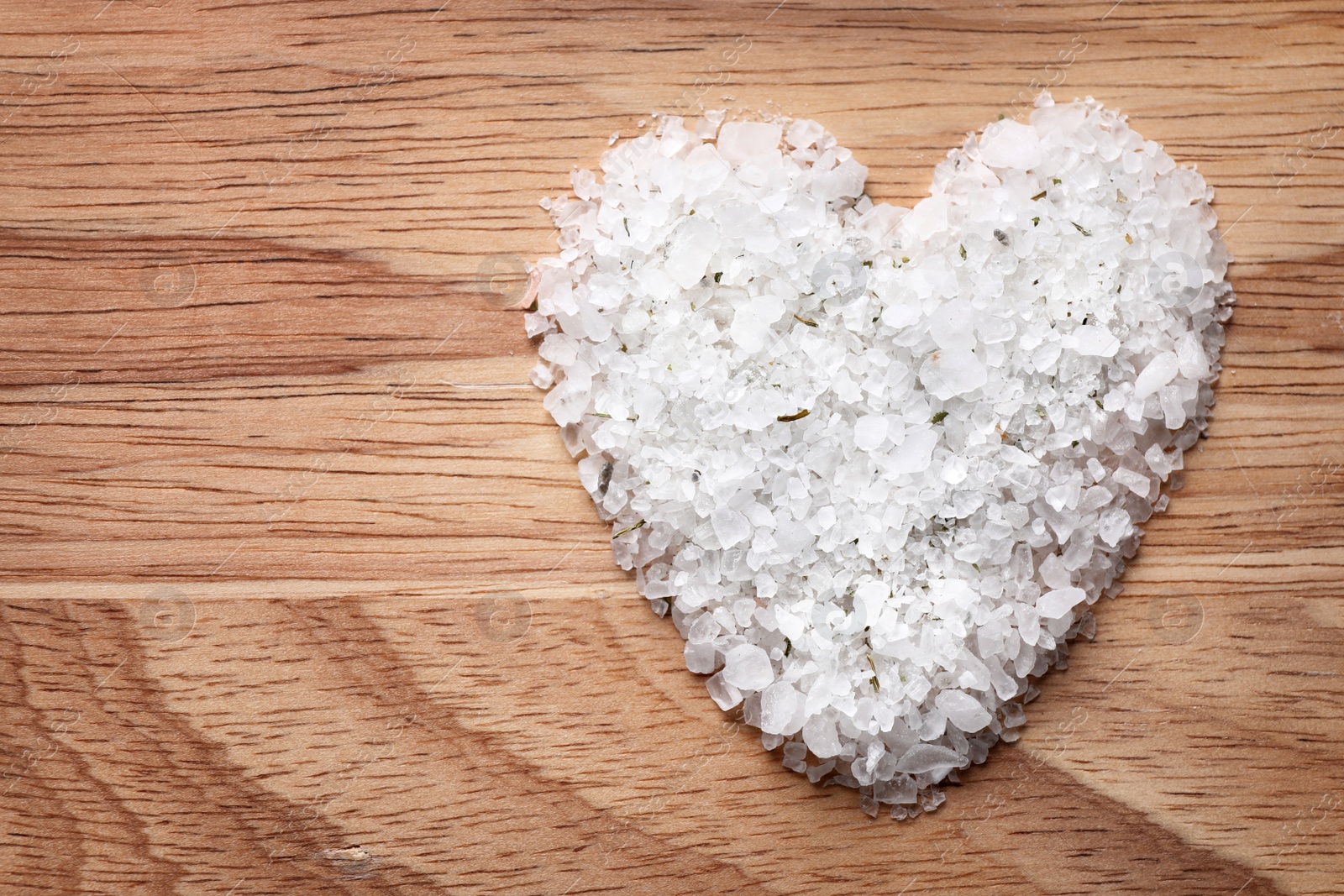 Photo of Heart made of white sea salt on wooden background, top view with space for text. Spa treatment