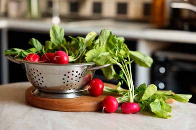 Metal colander with fresh radishes on white table