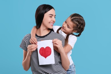 Photo of Happy woman with her cute daughter and handmade greeting card on light blue background. Mother's day celebration