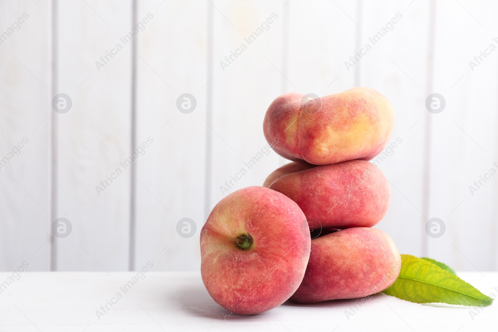 Photo of Fresh ripe donut peaches on white wooden table. Space for text