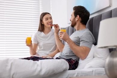 Photo of Tasty breakfast. Husband feeding his wife in bedroom