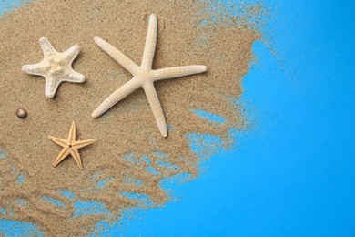 Photo of Beautiful starfishes and sand on blue background, flat lay. Space for text