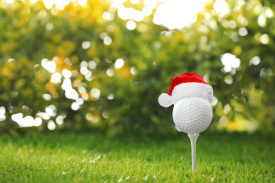 Image of Golf ball with small Santa hat on tee against blurred background. Space for text
