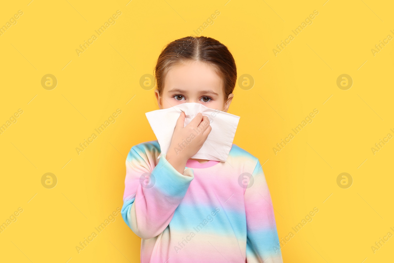 Photo of Girl blowing nose in tissue on orange background. Cold symptoms