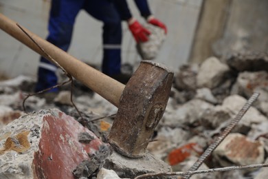 Photo of Sledgehammer on pile of broken stones. Man working outdoors, selective focus