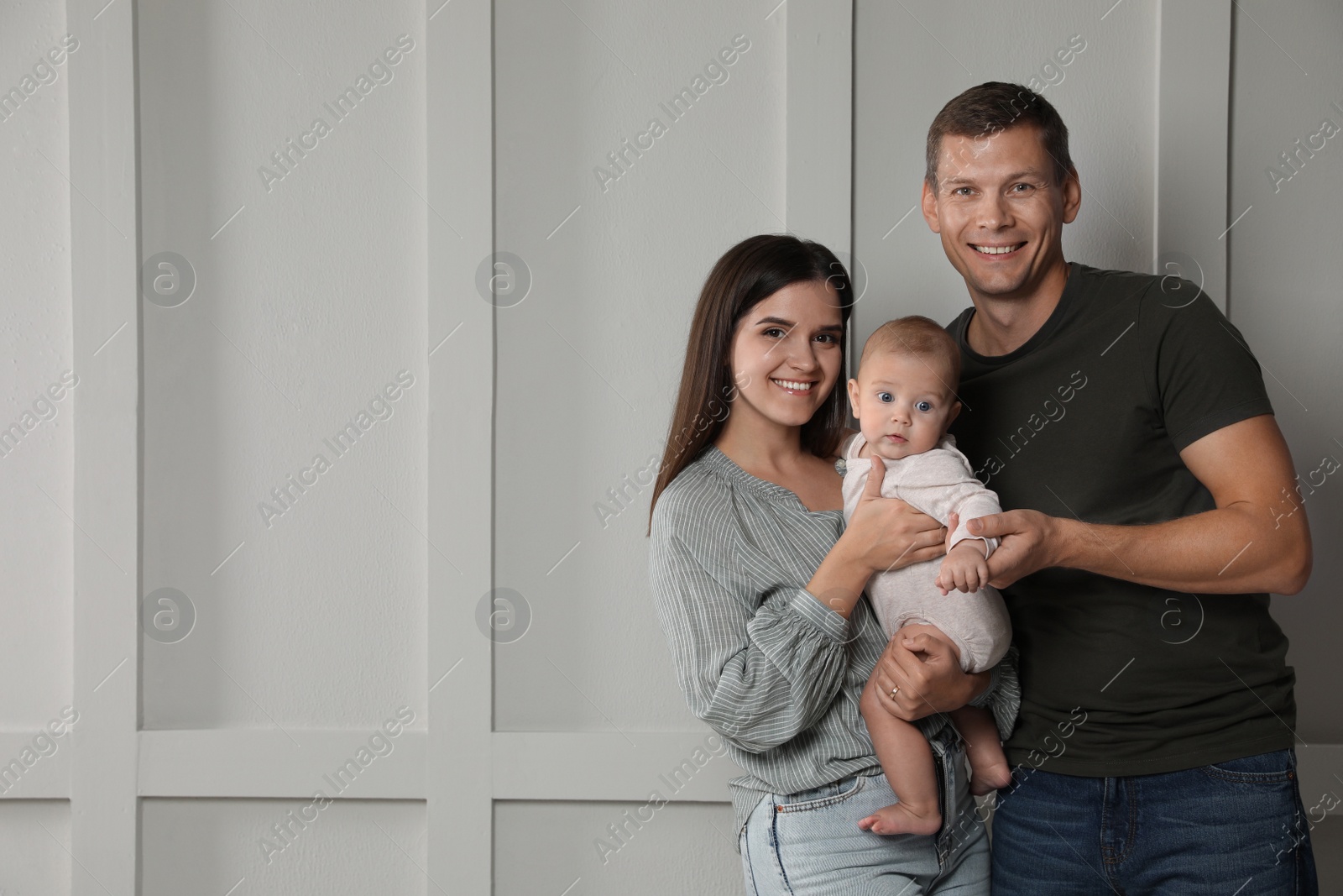 Photo of Happy family. Couple with their cute baby near light wall, space for text