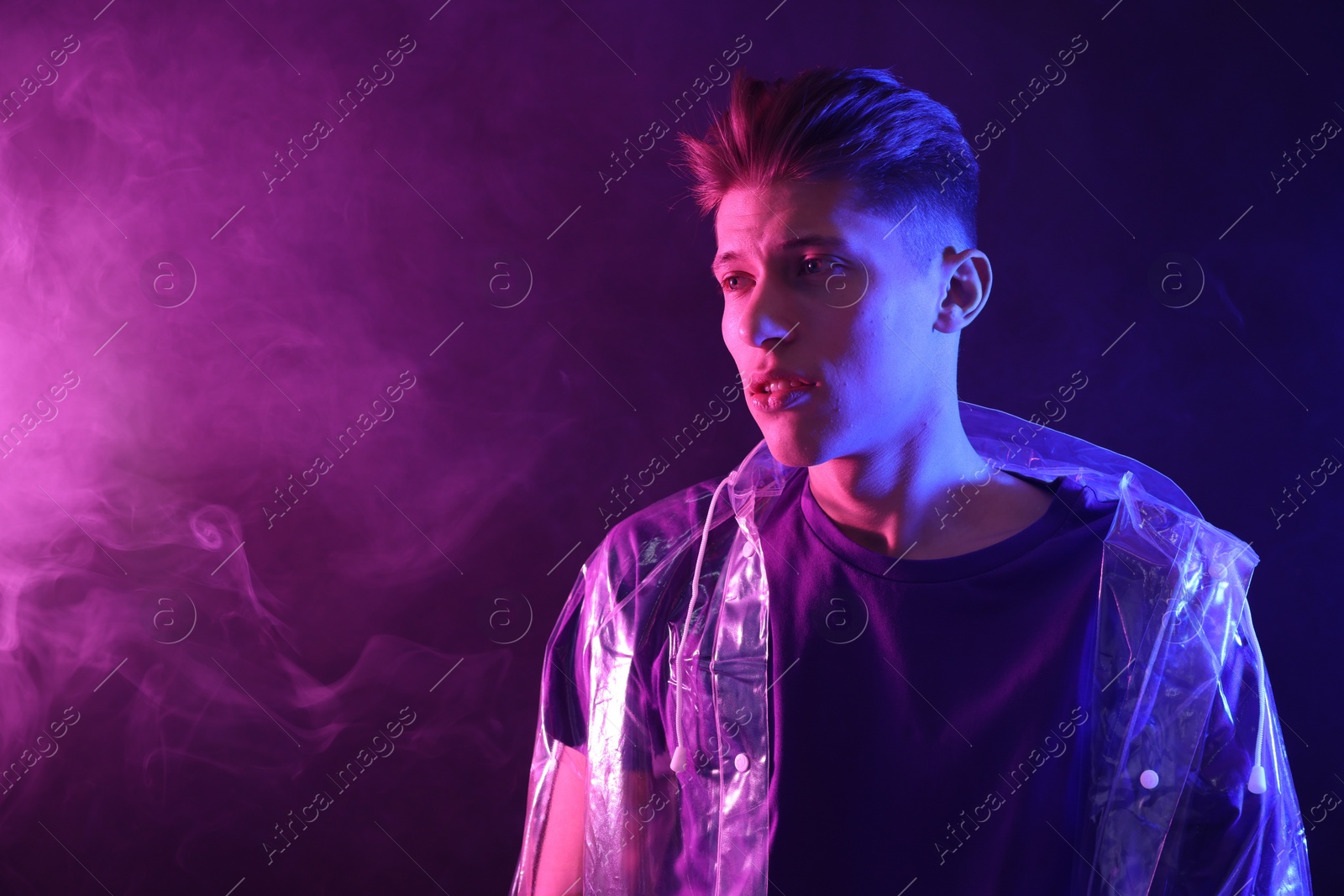 Photo of Young man wearing clear coat in neon lights with smoke effect. Space for text