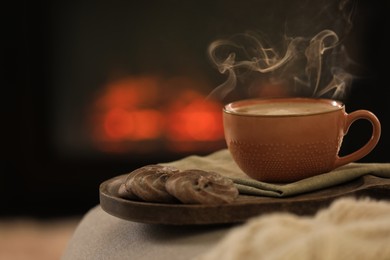 Photo of Hot drink and cookies near fireplace at home, space for text. Cozy atmosphere