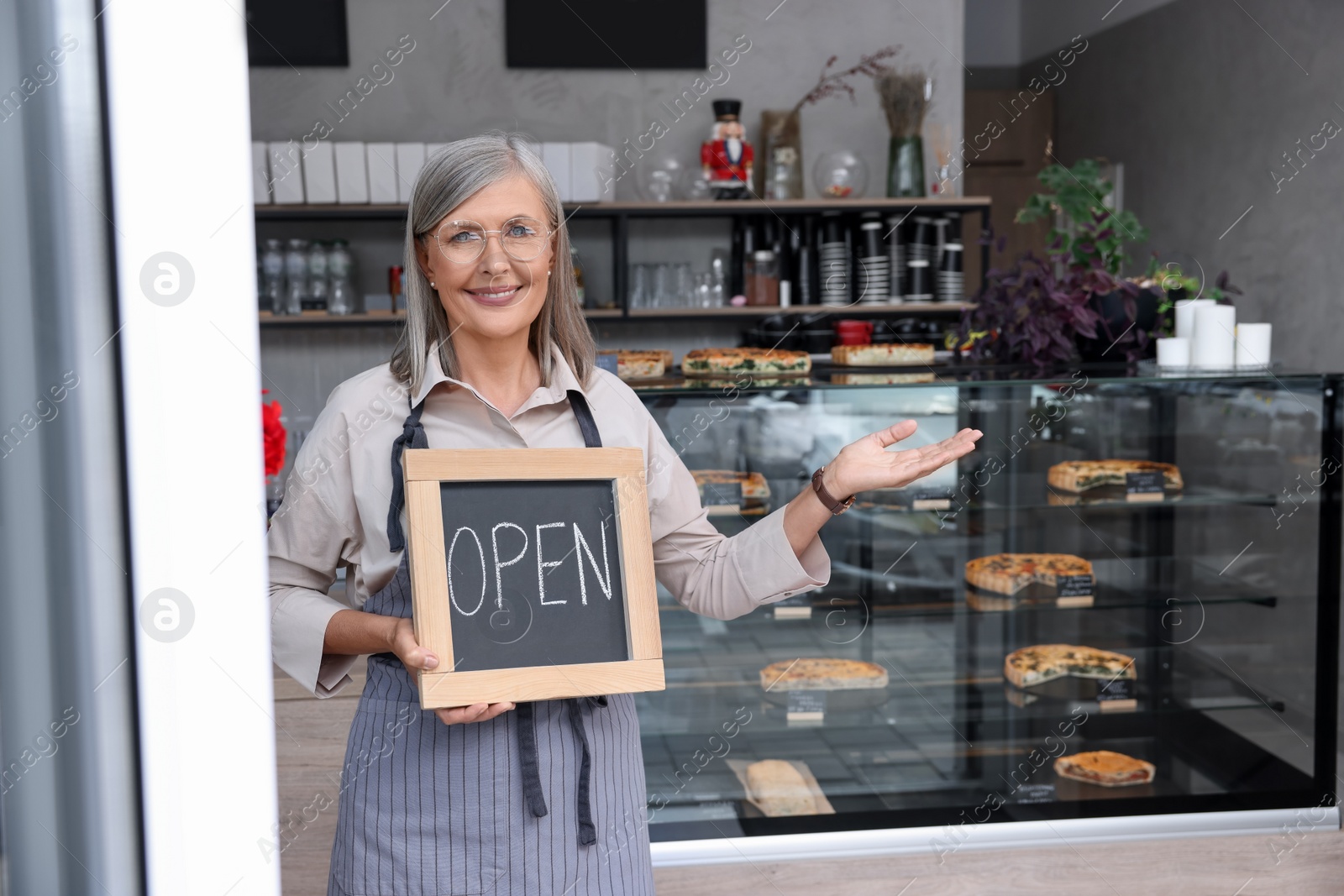 Photo of Happy business owner holding open sign and inviting to come into her cafe, space for text