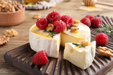 Photo of Brie cheese served with raspberries, walnuts and honey on wooden table, closeup