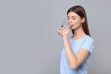 Photo of Healthy habit. Woman drinking fresh water from glass on grey background. Space for text