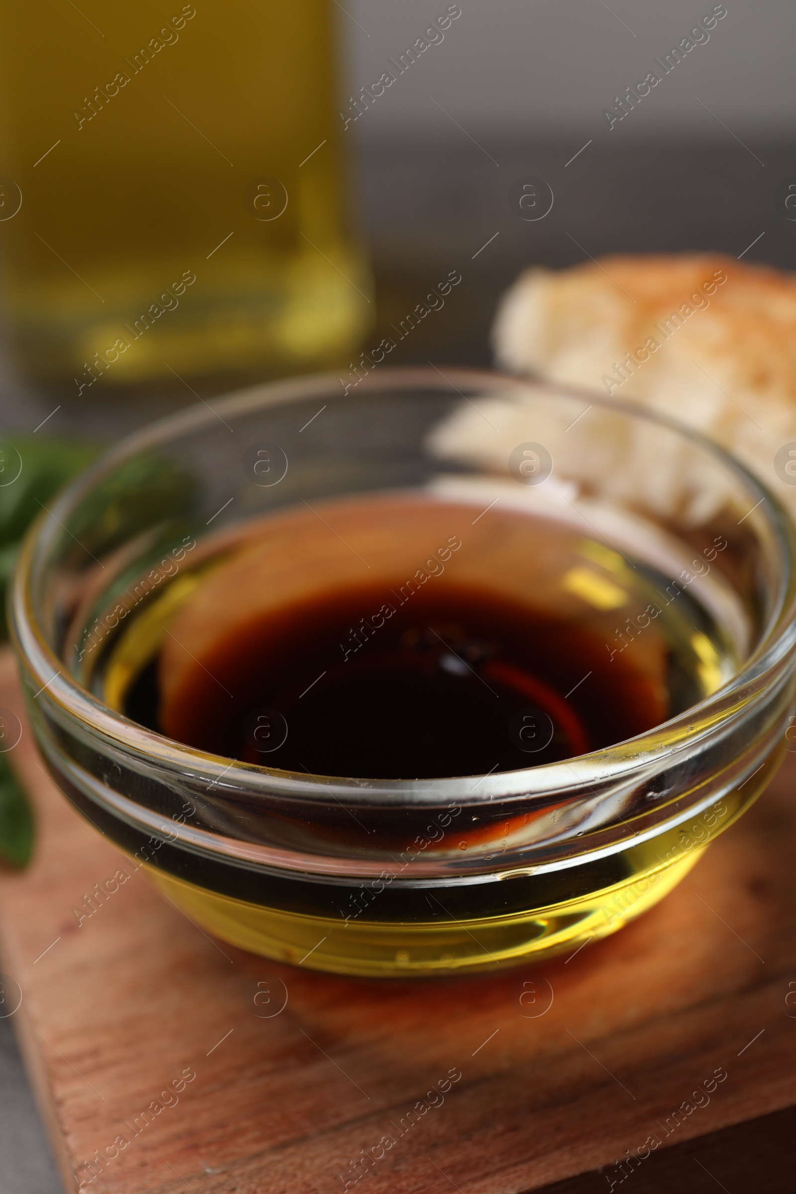 Photo of Bowl of organic balsamic vinegar with oil on wooden board, closeup