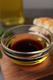 Photo of Bowl of organic balsamic vinegar with oil on wooden board, closeup