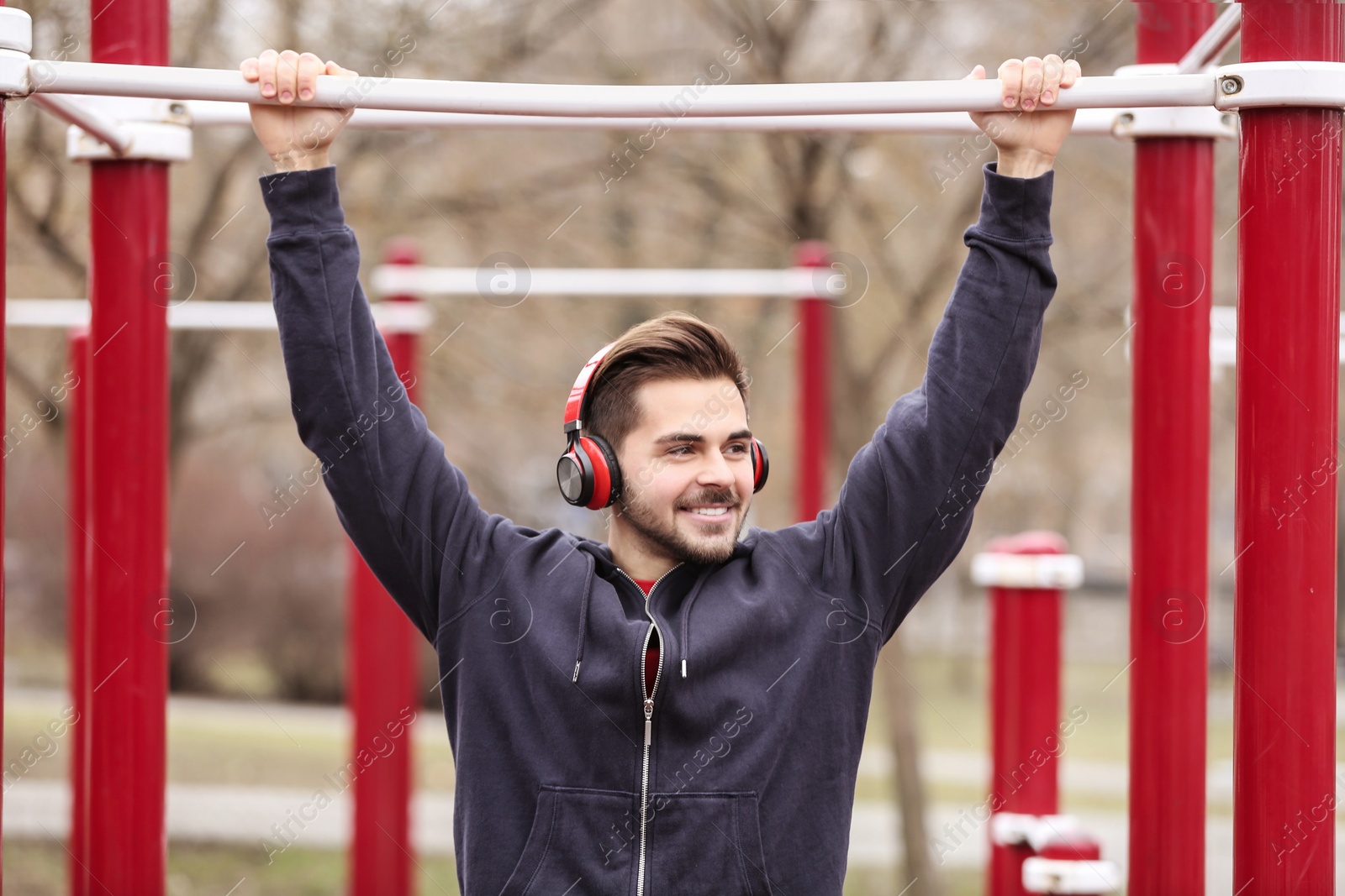 Photo of Young man with headphones listening to music and exercising on sports ground