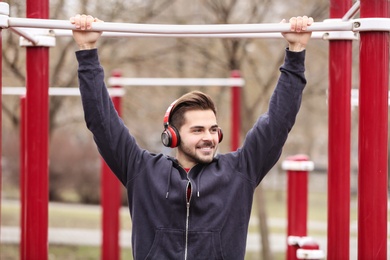 Photo of Young man with headphones listening to music and exercising on sports ground