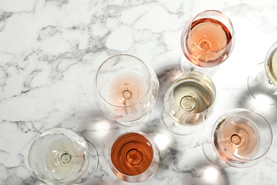 Different glasses with wine on marble background, flat lay